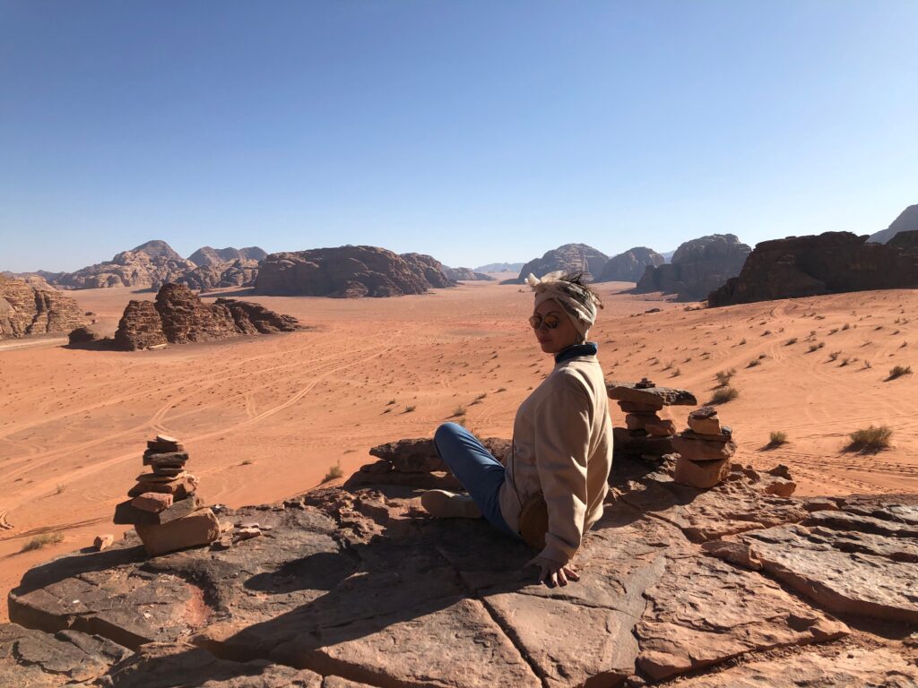 A person sits on a rocky ledge overlooking the vast Wadi Rum desert landscape.