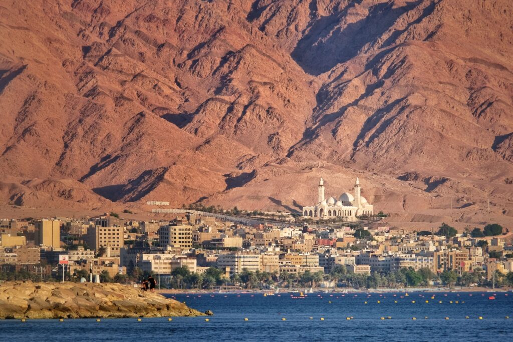 A scenic view of Aqaba city against a dramatic mountain backdrop by the sea.