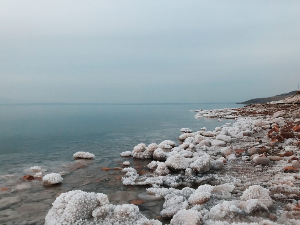 Peaceful scenery of calm Dead Sea with natural mineral salt formations and stones against cloudy sky